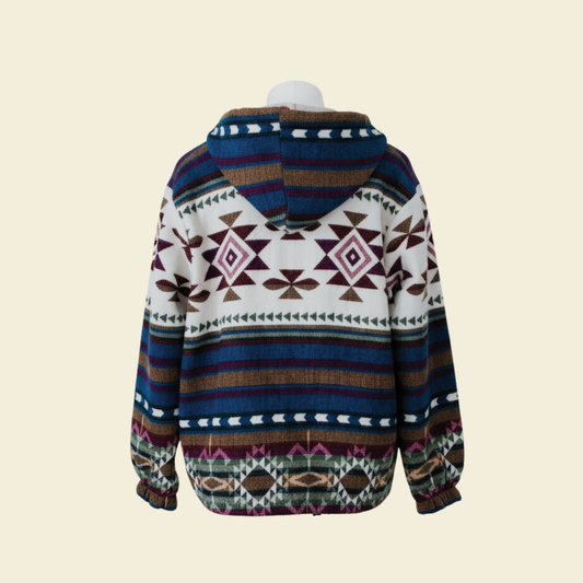 Back view of the WAYRA boho jacket made from a wool blend with alpaca, featuring colorful geometric Andean patterns in blue, green, purple, brown, and cream. Photographed against a solid cream background.